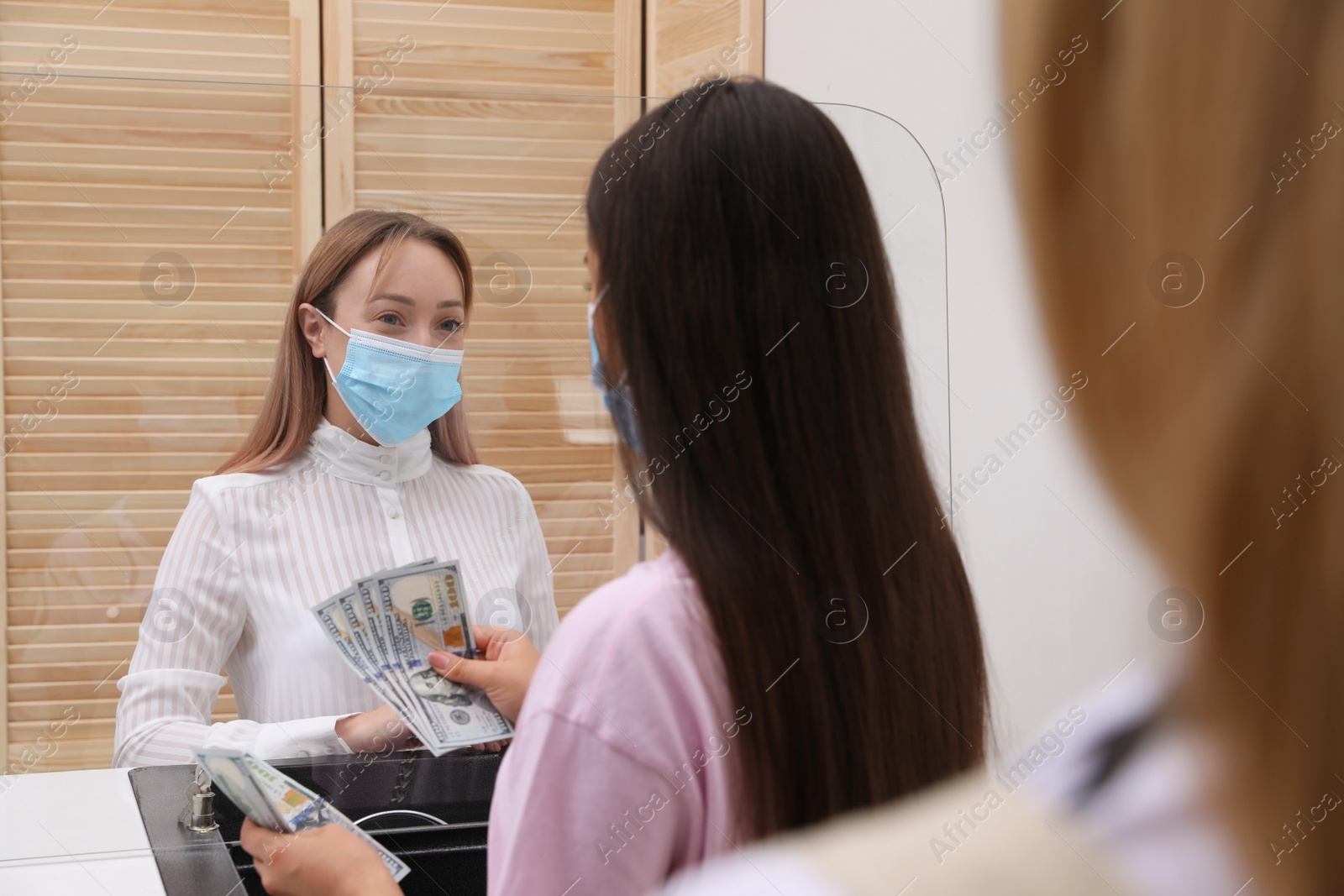 Photo of Woman with protective mask counting money at cash department window in bank. Currency exchange