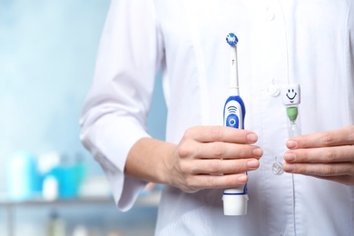 Dentist with electric toothbrush and sand glass at workplace, closeup