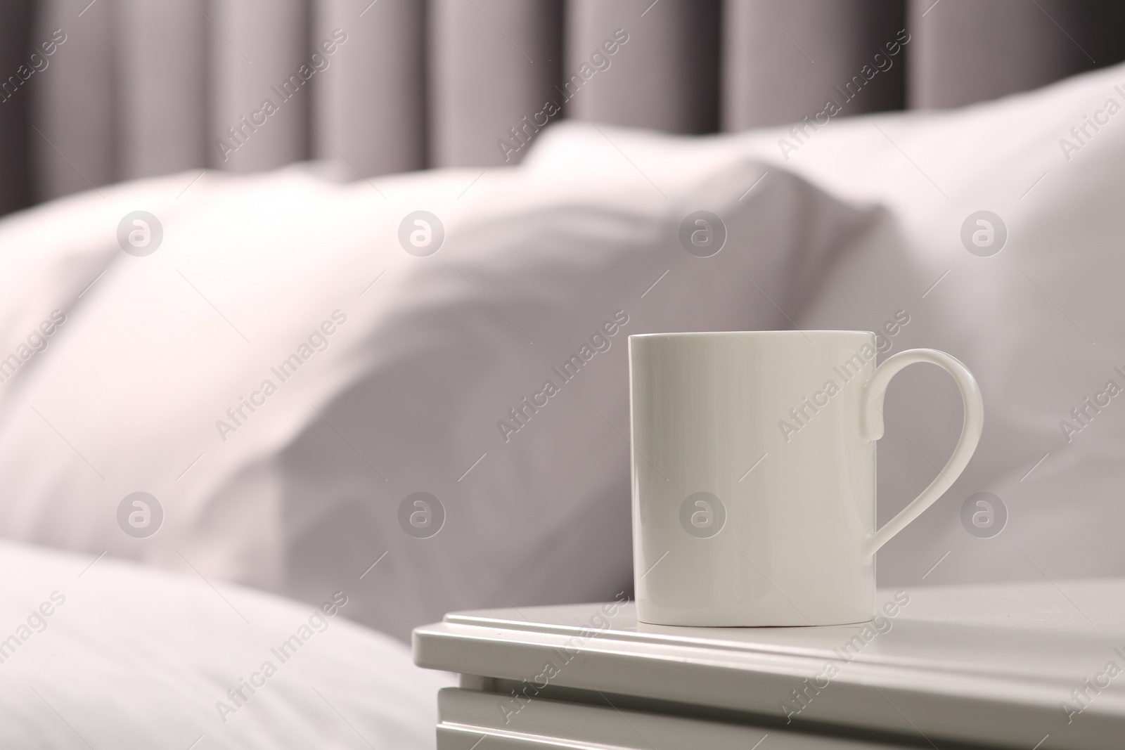 Photo of Ceramic mug on white bedside table indoors. Mockup for design