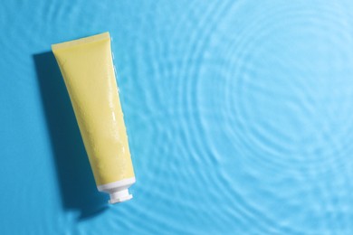 Photo of Tube with moisturizing cream in water on light blue background, top view. Space for text