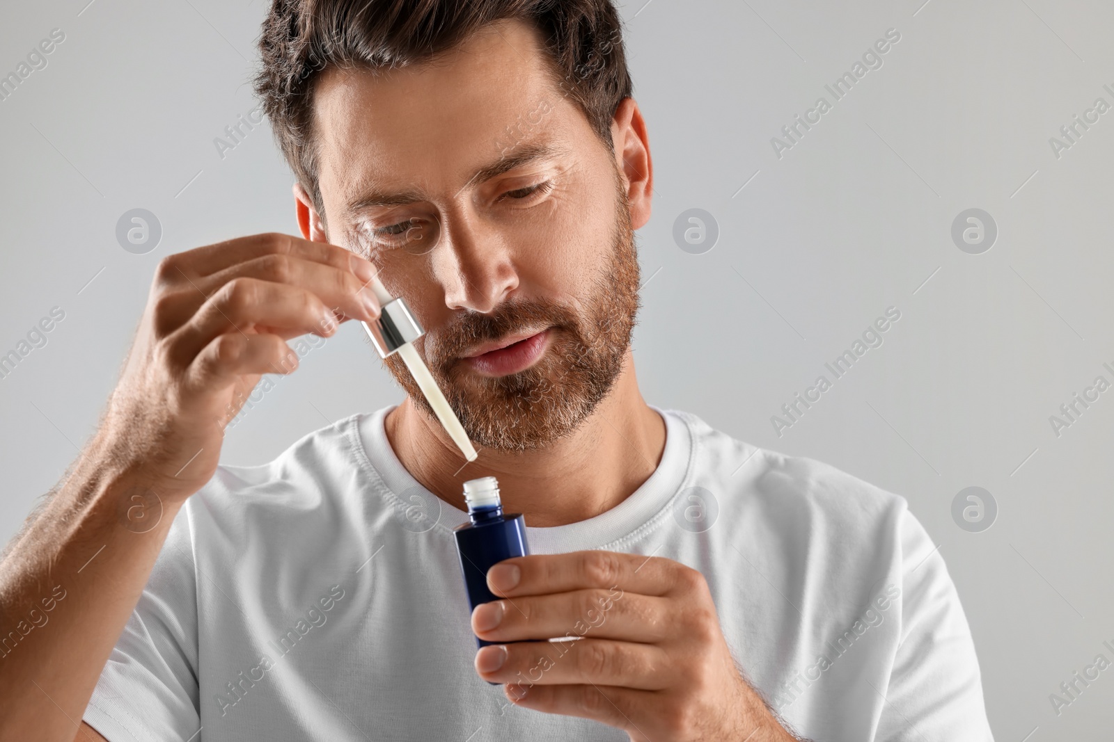 Photo of Handsome man with cosmetic serum on light grey background