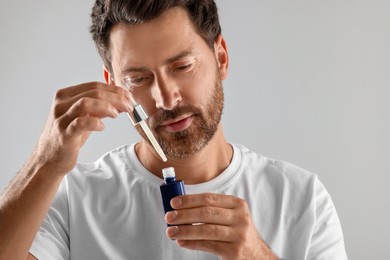 Handsome man with cosmetic serum on light grey background