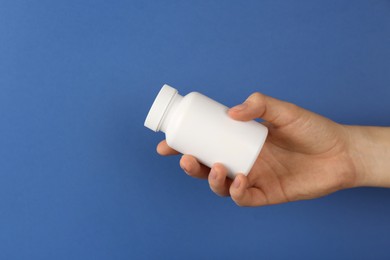 Photo of Woman holding blank white jar of vitamins on blue background, closeup. Space for text