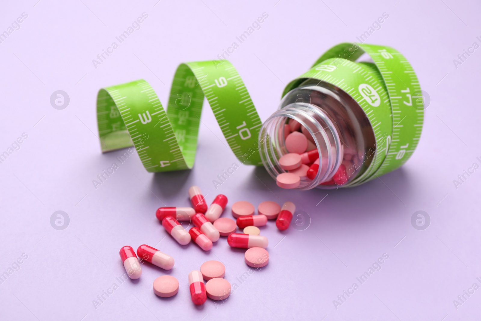 Photo of Jar of weight loss pills and measuring tape on violet background