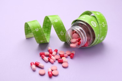 Photo of Jar of weight loss pills and measuring tape on violet background