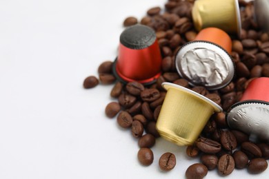 Many coffee capsules and beans on white table, closeup. Space for text