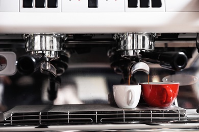 Photo of Aromatic coffee pouring into cups from modern machine, closeup