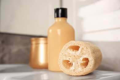 Photo of Natural loofah sponge and cosmetic products on washbasin in bathroom, closeup