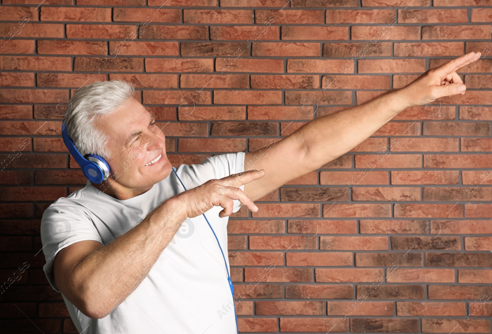 Photo of Mature man enjoying music in headphones against brick wall