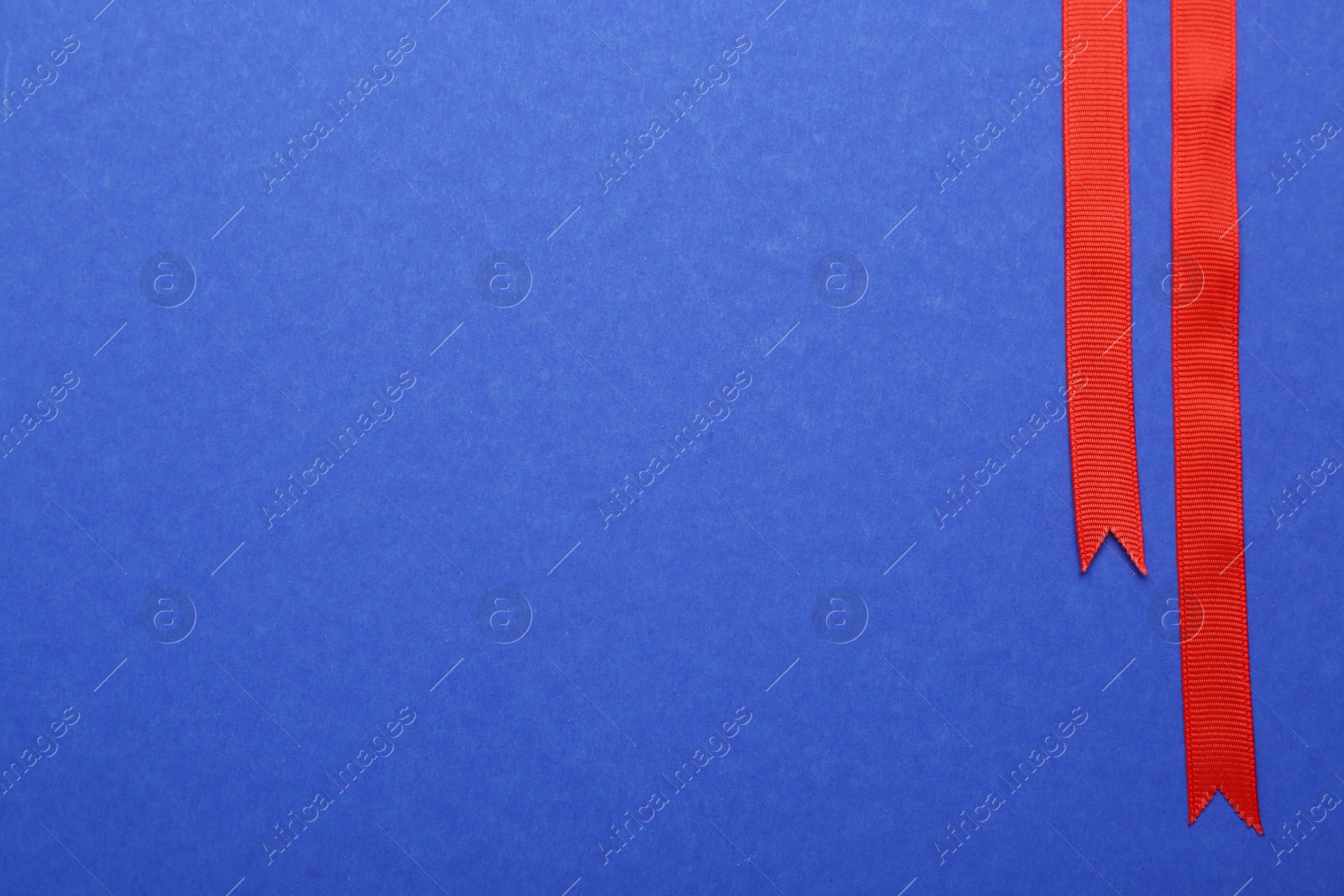 Photo of Beautiful red ribbons on blue background, flat lay. Space for text