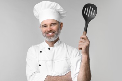 Happy chef in uniform with spatula on grey background