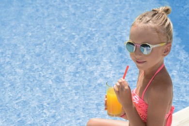 Photo of Cute little girl with glass of juice near swimming pool on sunny day. Space for text