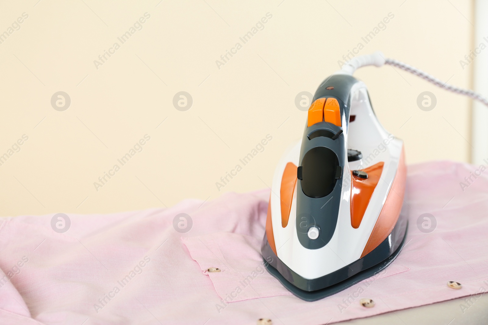 Photo of Board with modern iron and shirt on beige background, space for text. Laundry day