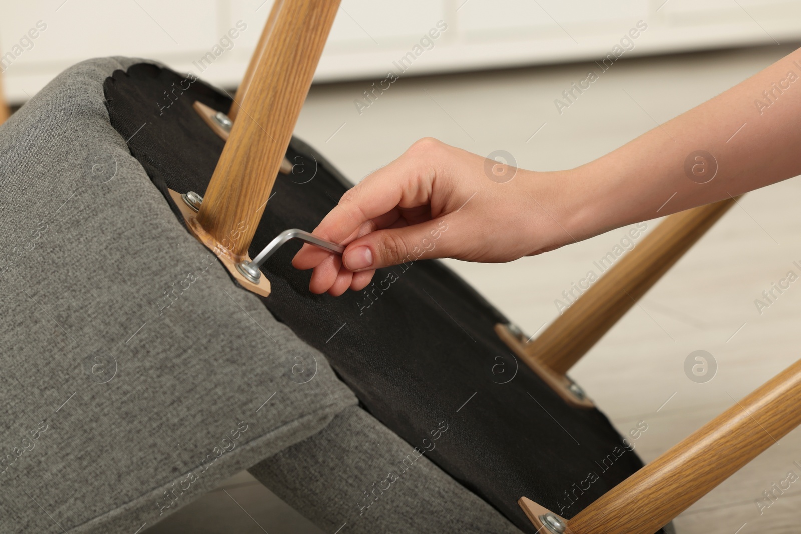 Photo of Woman with hex key assembling armchair on floor indoors, closeup