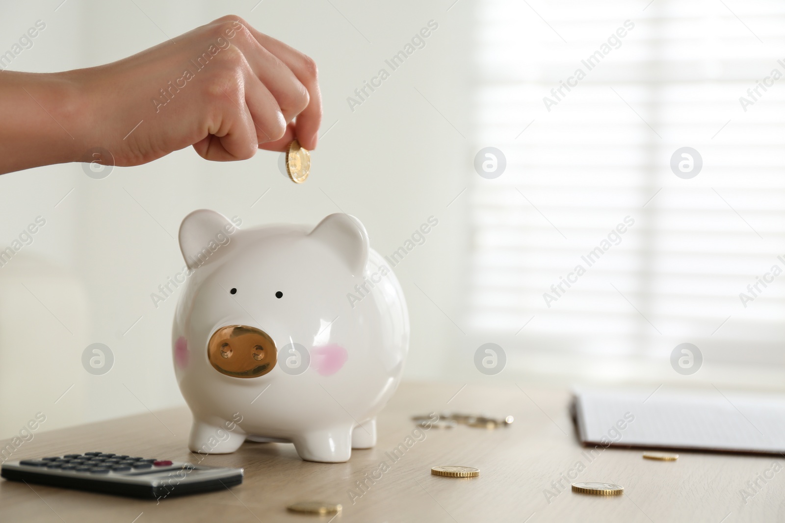 Photo of Woman putting money into piggy bank at wooden table indoors, closeup. Space for text