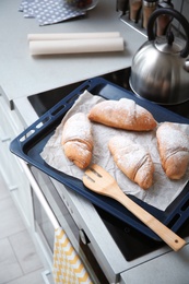 Baking tray with tasty croissants on stove