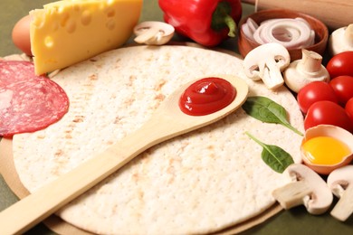 Photo of Pizza base, spoon with tomato sauce and products on green table, closeup
