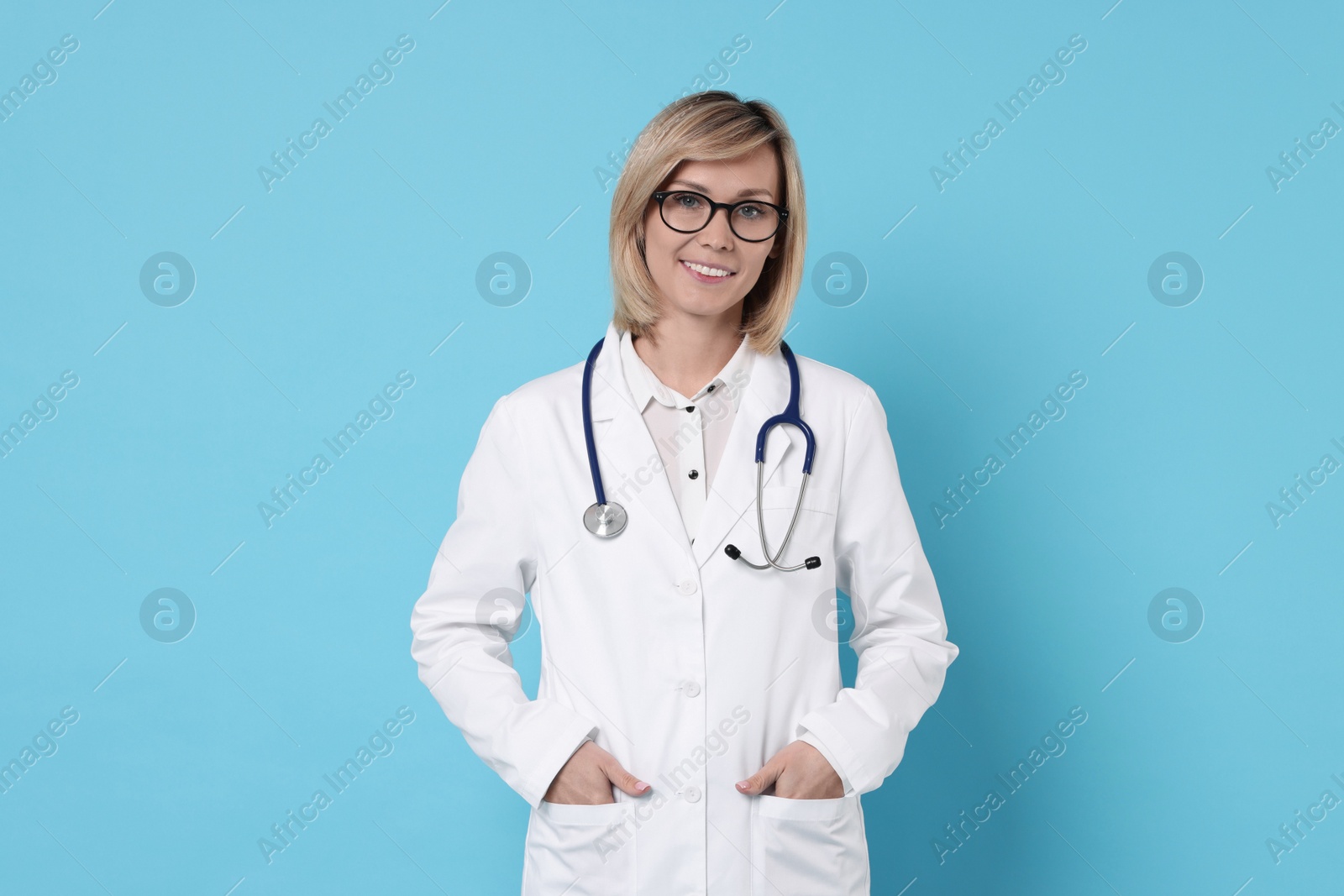 Photo of Smiling doctor with stethoscope on light blue background