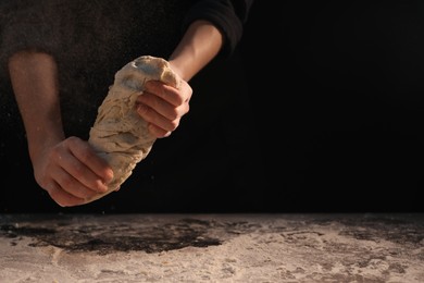 Photo of Making bread. Woman kneading dough at table on dark background, closeup. Space for text