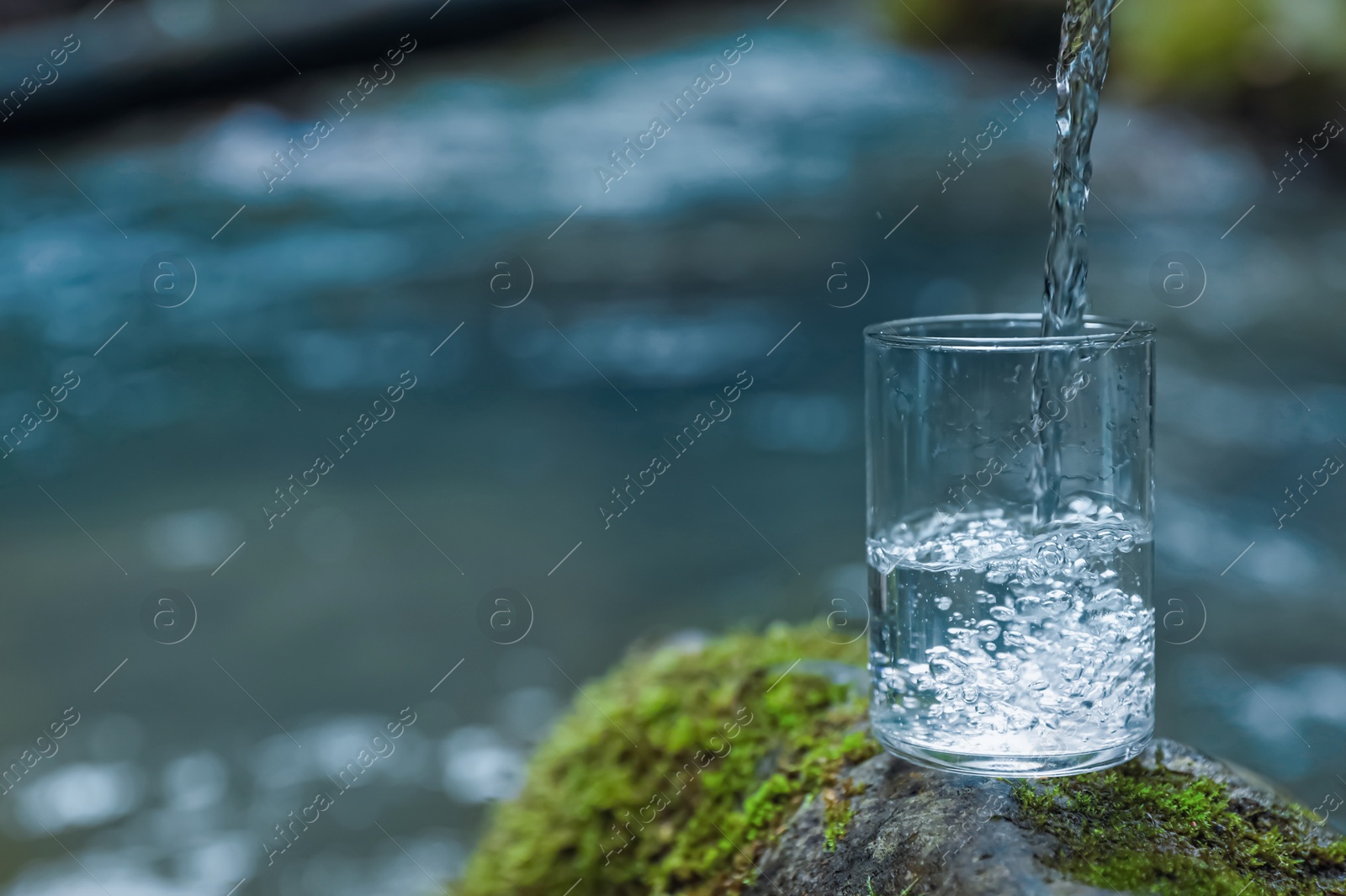 Photo of Fresh water pouring into glass on stone near river. Space for text