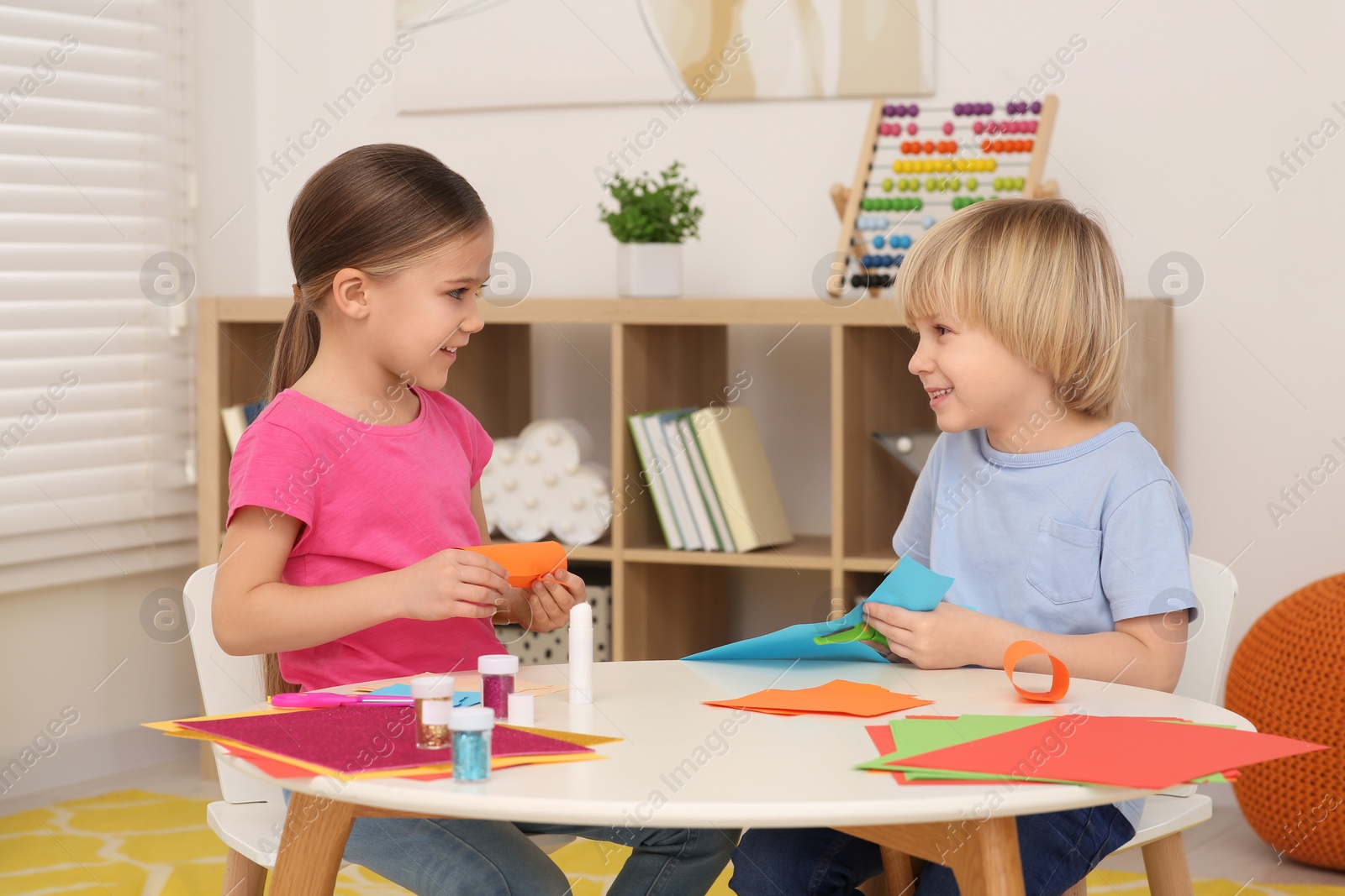 Photo of Cute children making paper toys at desk in room. Home workplace