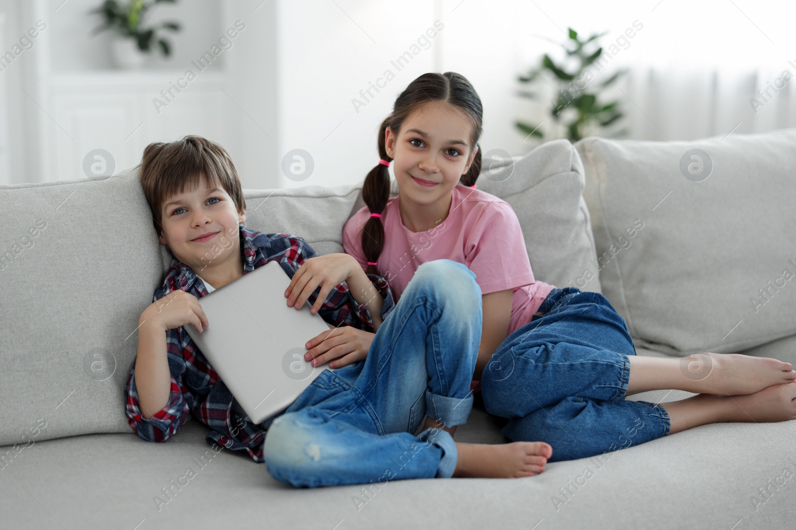 Photo of Happy brother and sister with tablet on sofa at home