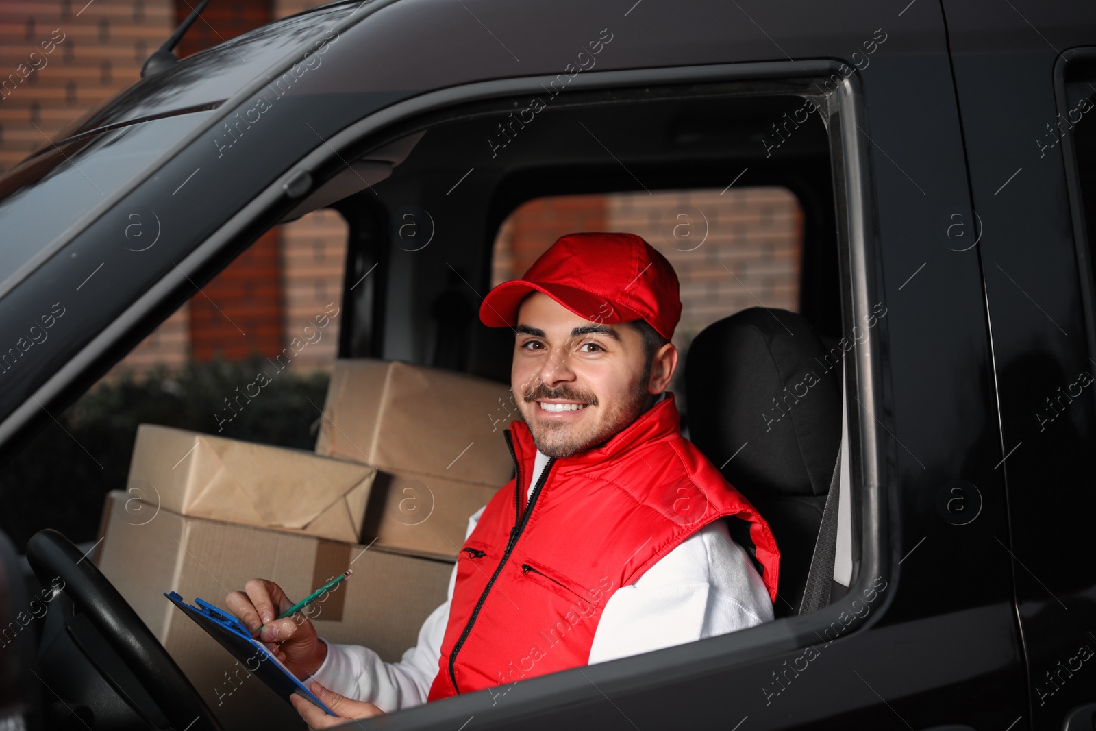 Photo of Deliveryman with clipboard and parcels in car