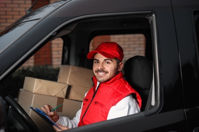 Photo of Deliveryman with clipboard and parcels in car