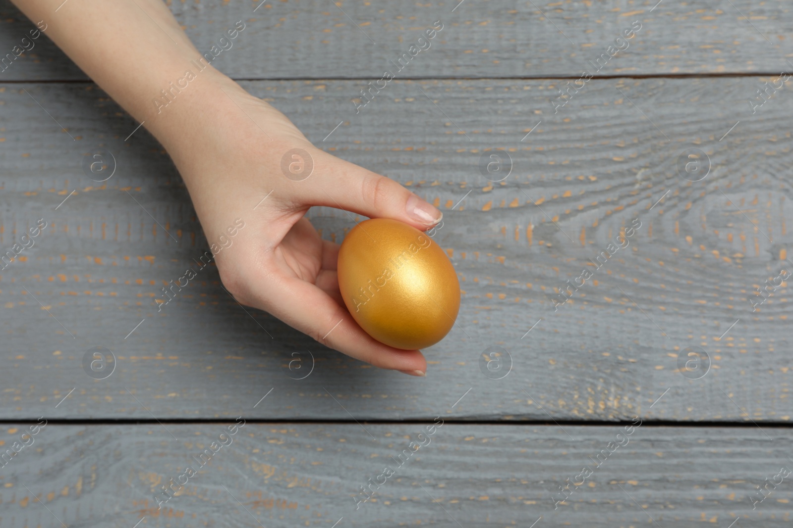 Photo of Woman holding shiny golden egg at grey wooden table, top view
