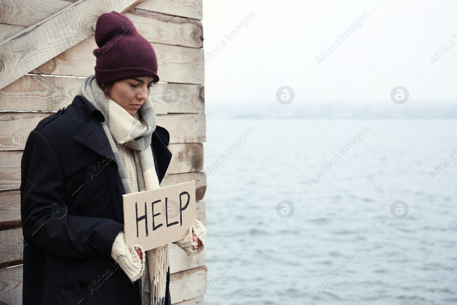 Photo of Poor young woman with HELP sign at riverside. Space for text