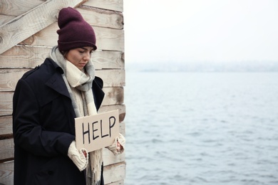 Poor young woman with HELP sign at riverside. Space for text