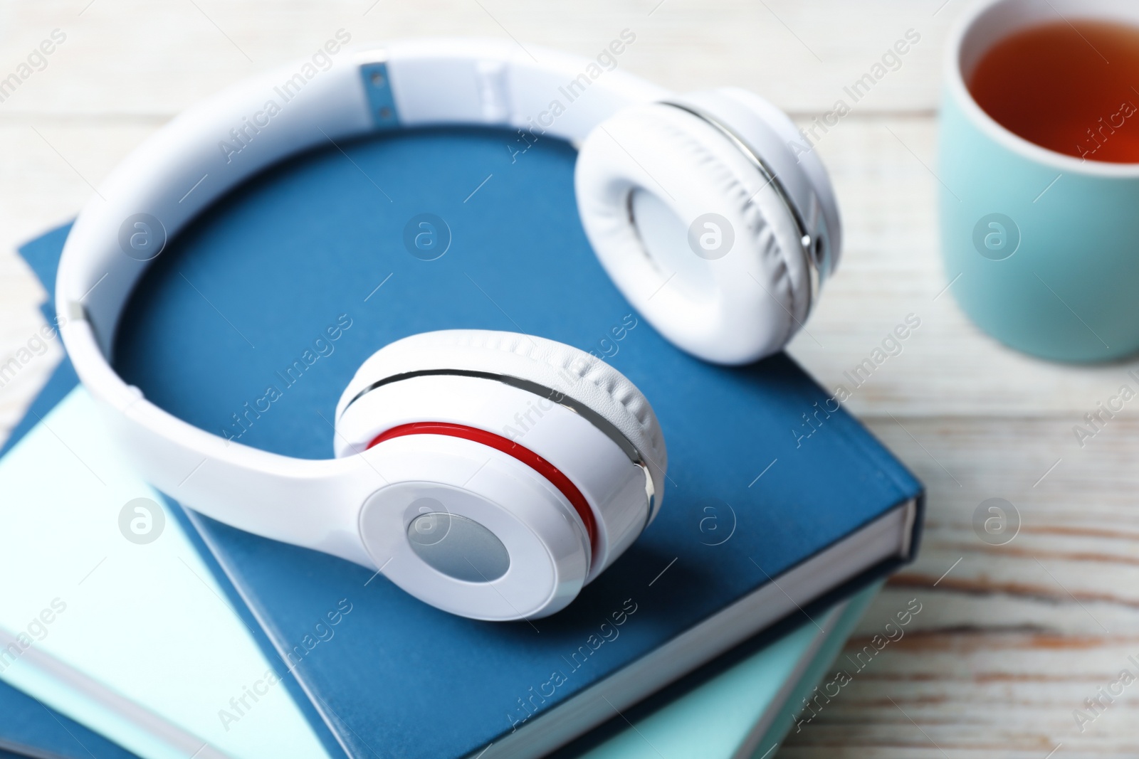 Photo of Modern headphones with hardcover books on wooden table, closeup