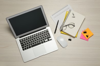 Modern laptop, glasses and office stationery on white wooden table, flat lay. Distance learning