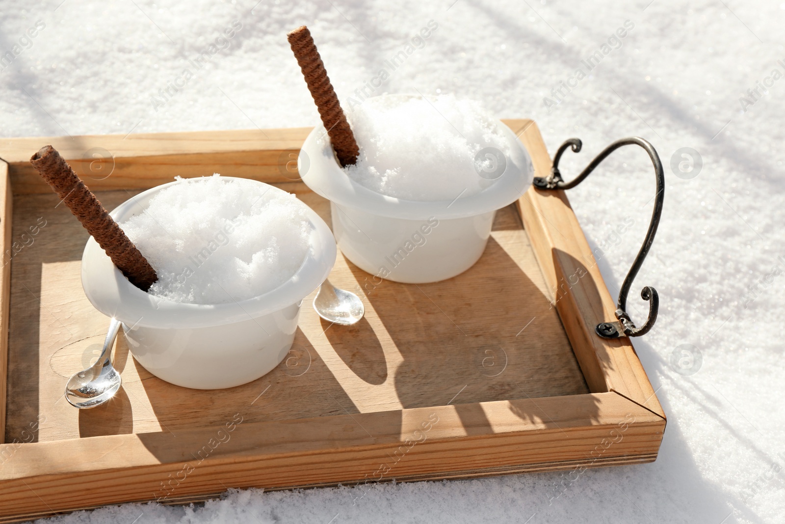 Photo of Tray with bowls of tasty ice cream and waffle rolls on snow