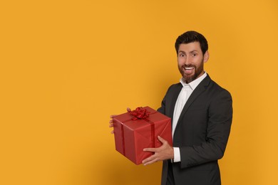 Photo of Handsome man holding gift box on yellow background, space for text