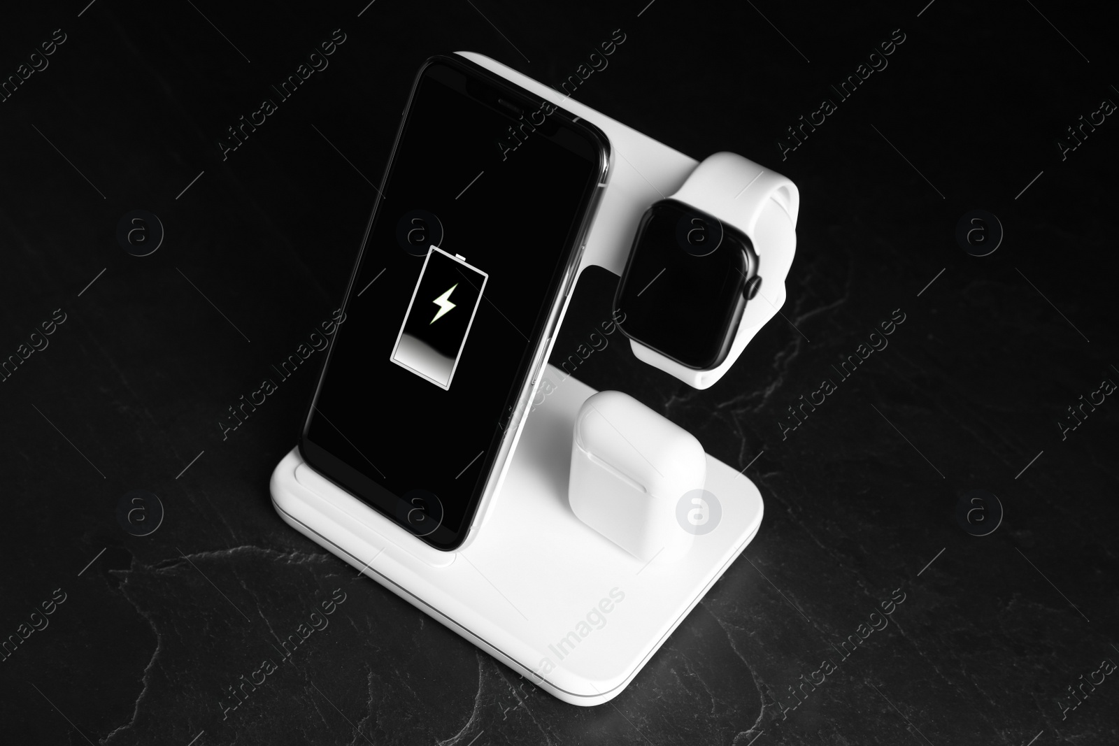 Photo of Set of gadgets charging with wireless pad on black stone table