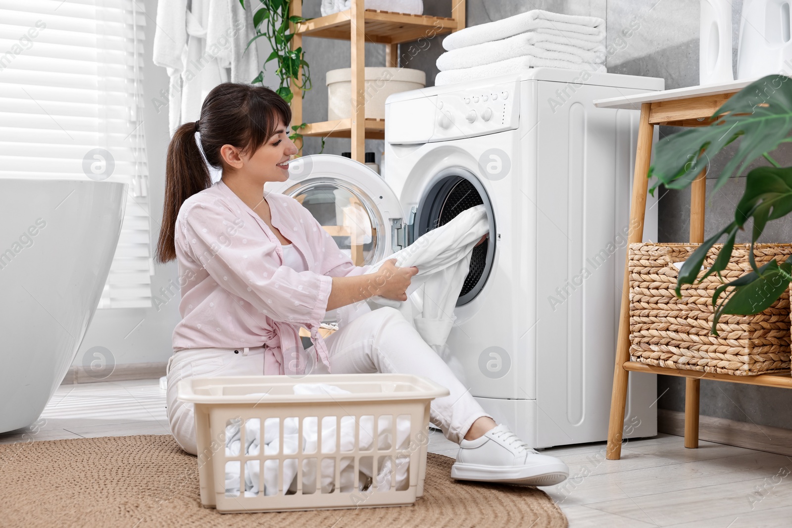 Photo of Happy young housewife putting laundry into washing machine at home