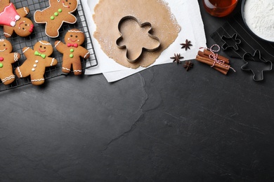 Flat lay composition with homemade gingerbread man cookies on black table, space for text