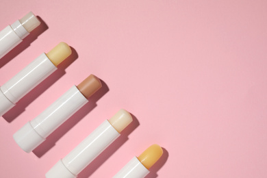 Hygienic lipsticks on pink background, flat lay. Space for text