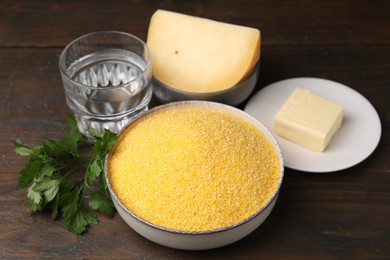 Raw cornmeal in bowl, cheese, butter, parsley and water on wooden table
