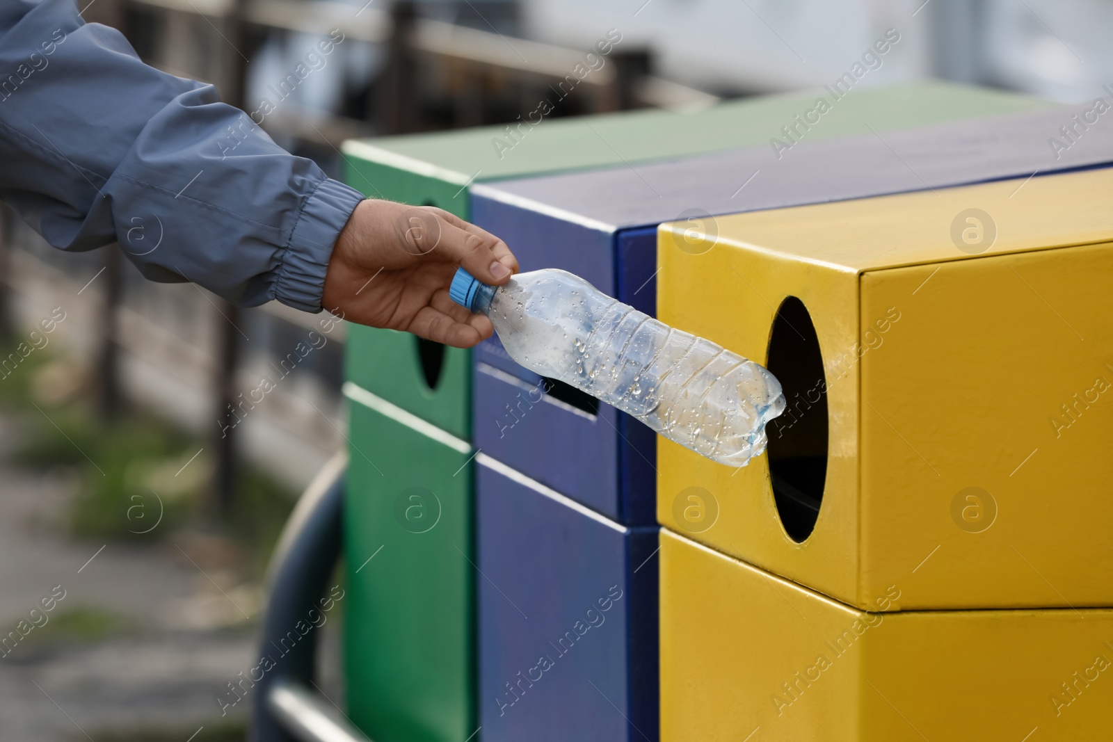 Photo of Man throwing plastic bottle into garbage bin outdoors, closeup. Waste sorting