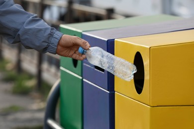 Man throwing plastic bottle into garbage bin outdoors, closeup. Waste sorting