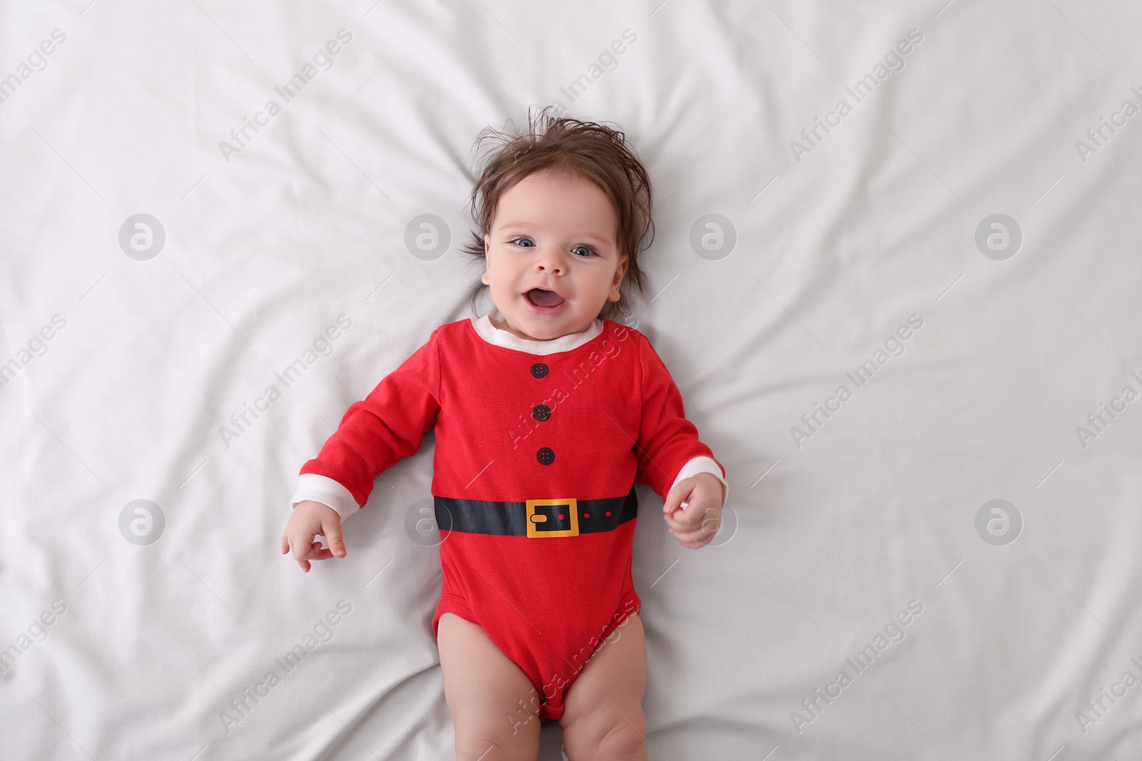 Photo of Cute baby wearing festive Christmas costume on white bedsheet, top view