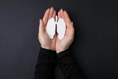 Photo of Quitting smoking concept. Woman holding paper lungs on black background, top view