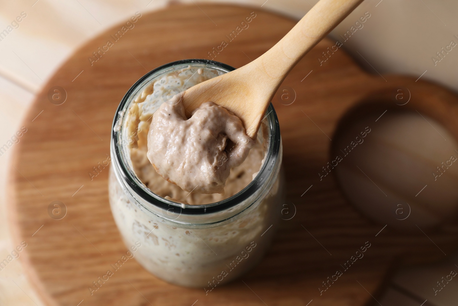 Photo of Taking sourdough starter with spoon at table, closeup