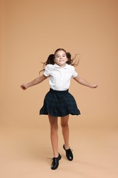 Cute schoolgirl jumping on beige background, space for text