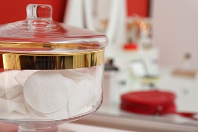 Glass jar with cotton pads near makeup table in room