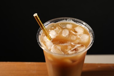 Refreshing iced coffee with milk in takeaway cup on table against black background, closeup