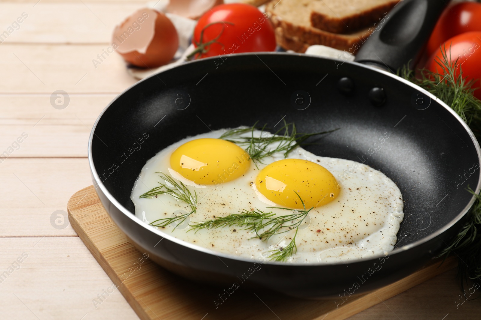 Photo of Frying pan with tasty cooked eggs, dill and other products on light wooden table, closeup