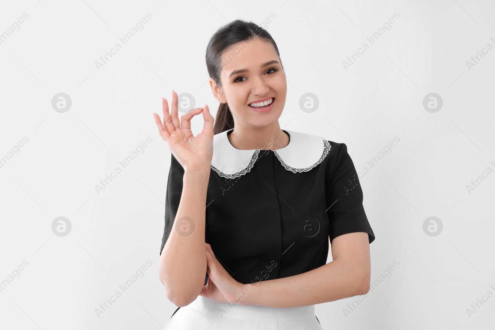 Photo of Young maid showing OK gesture on light background